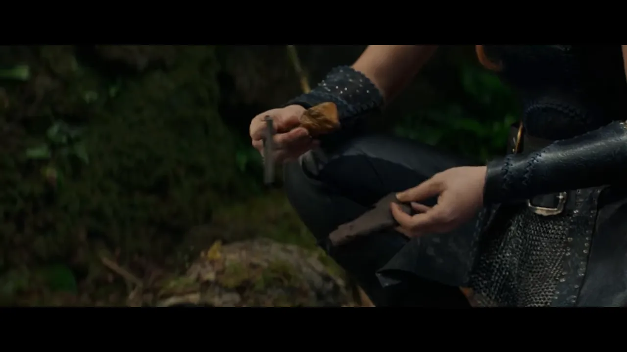 Close-up of hands holding a flint/metal tool and a wrapped object in a forest setting.