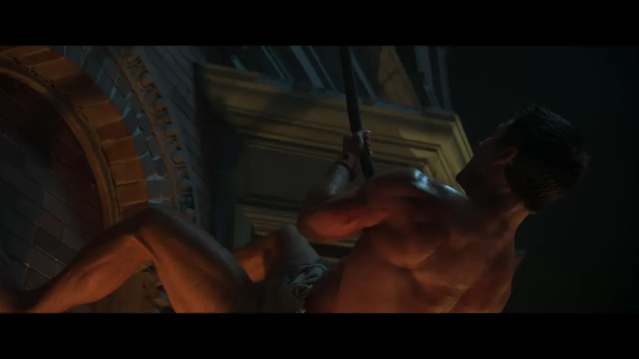 Man in a towel climbing the exterior of a building at night, gripping a rope.