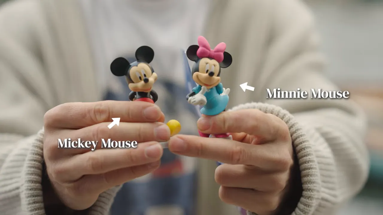 Close-up of hands holding small Mickey and Minnie figurines for tactile identification.