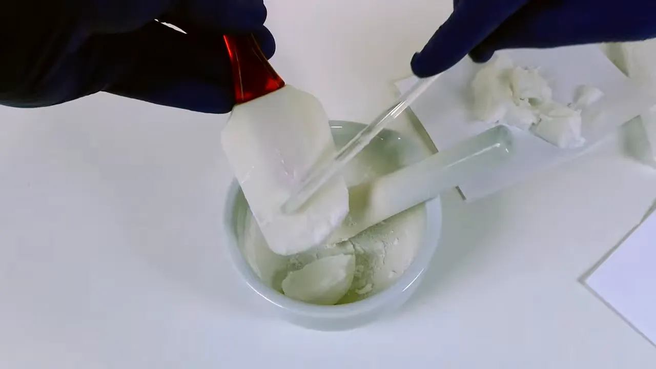 Espátula añadiendo porciones de emulsión blanca al mortero con pistilo en el interior