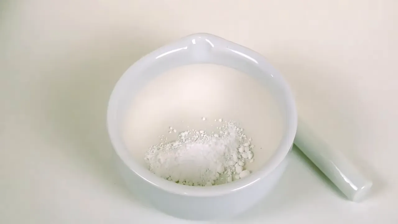 Mortero blanco con polvo mientras se pulveriza con pistilo y guantes azules