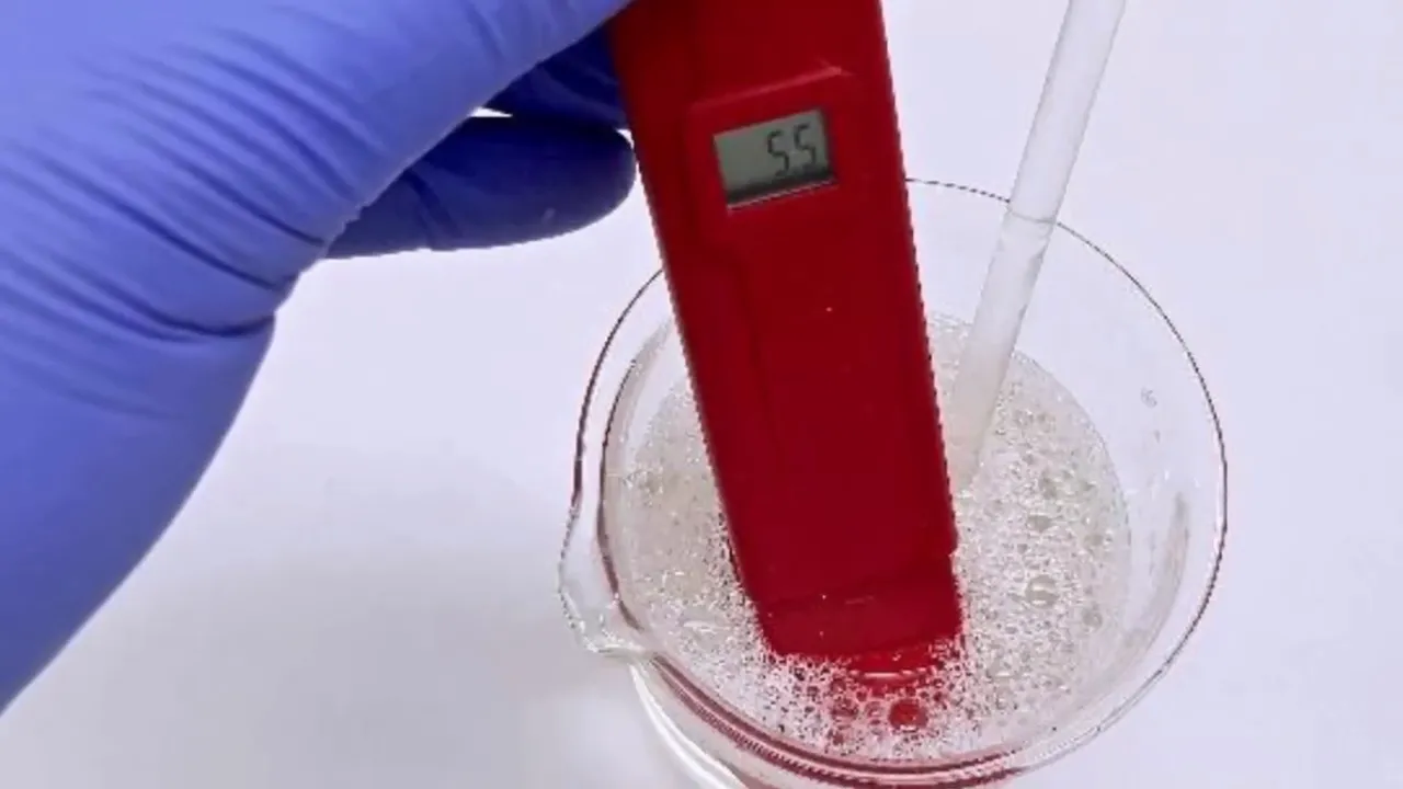 Medidor digital de pH marcando 5.5 en un vaso de precipitados con gel espumoso; mano con guante azul