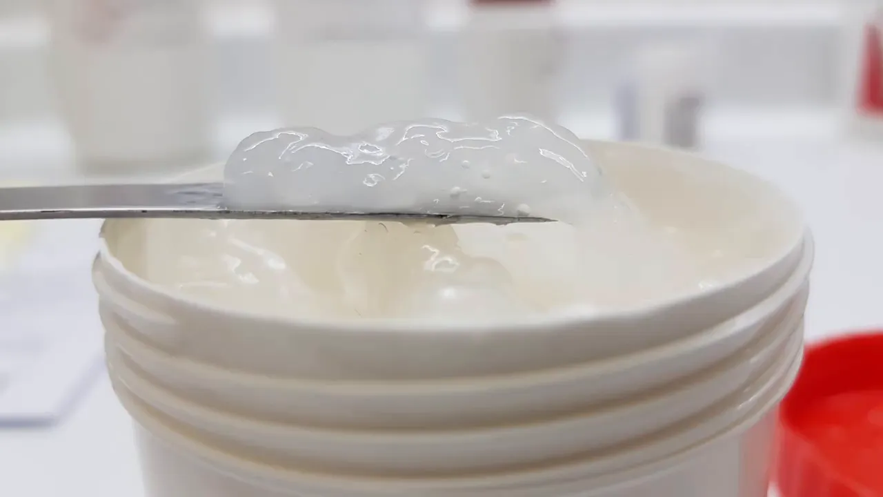 Pomada bucal blanca sobre espátula y tarro mostrando una textura homogénea y mucoadhesiva