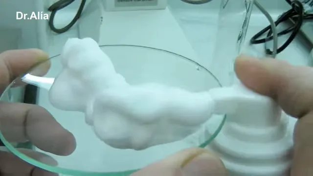 Espuma blanca y cremosa dispensada sobre una placa de vidrio junto a un envase espumador blanco