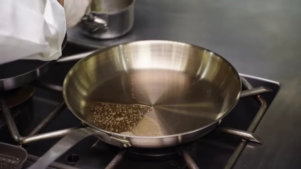 Beef fat melting and heating in a stainless steel skillet over a gas flame