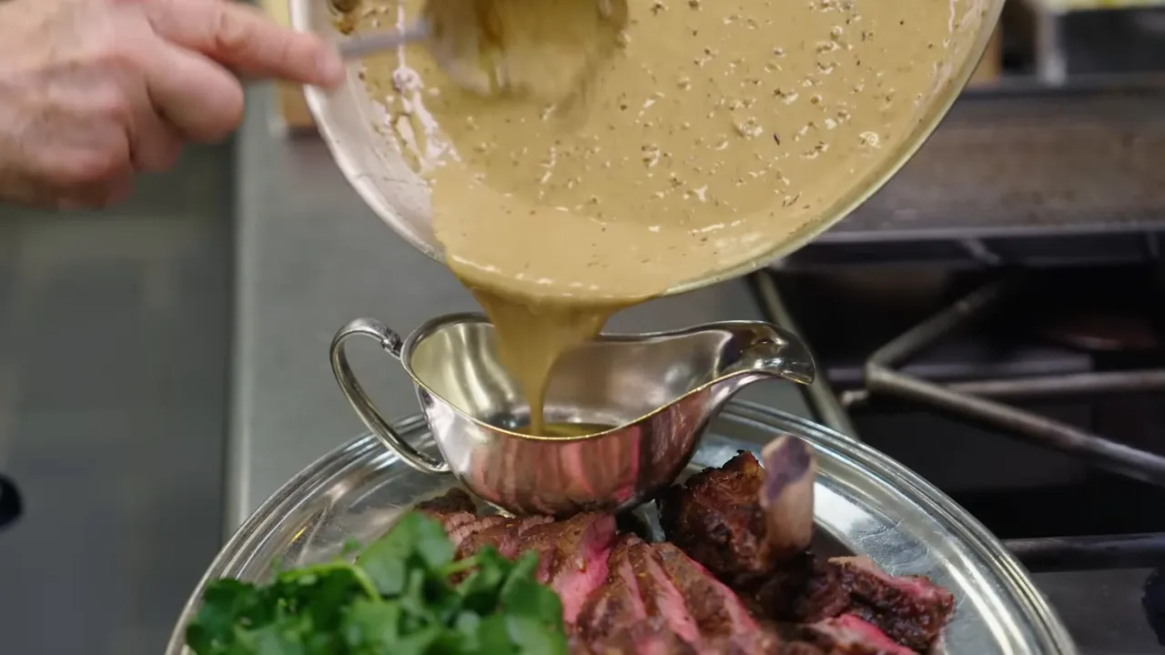 Au poivre pan sauce being poured over plated steak with greens and potato cake