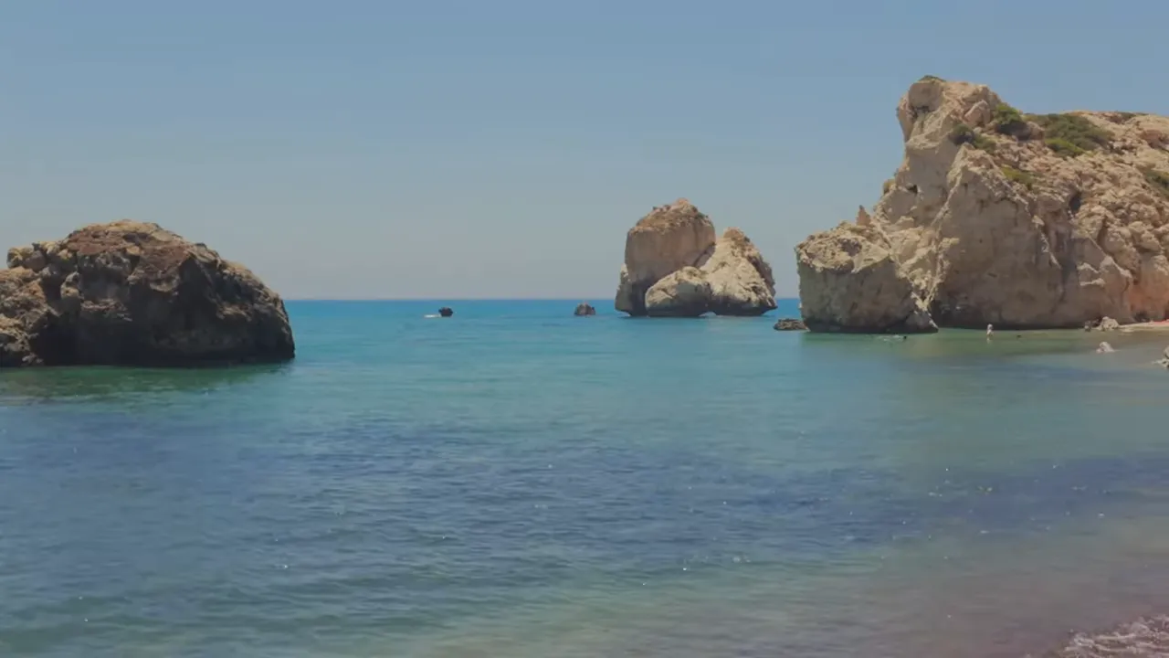 Large coastal rock formations in clear blue water at a pebbly beach