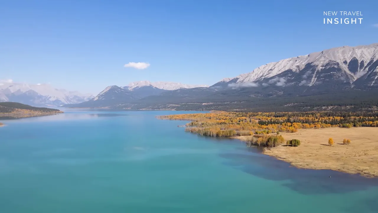 Aerial view of Abraham Lake with turquoise water, sandy shoreline, and mountain range in the distance