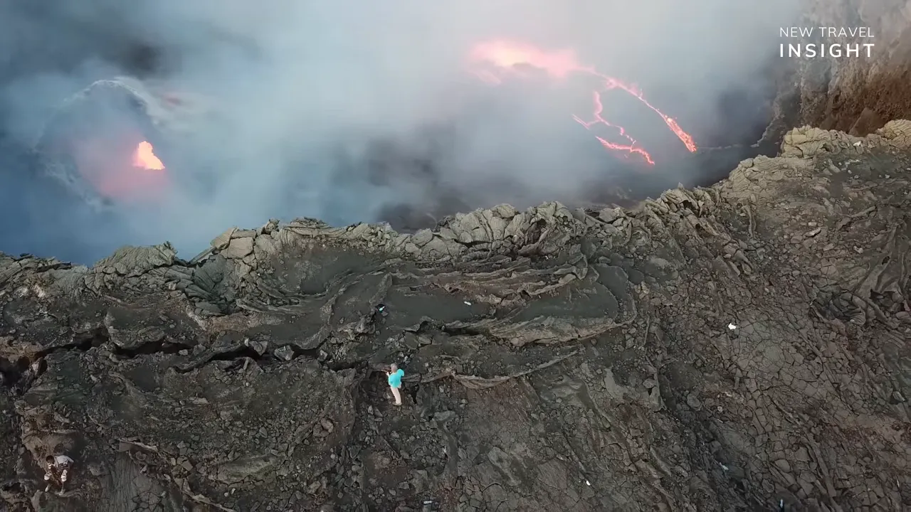 Person standing on volcanic rocks as a lava lake glows with red and pink fissures through smoke at Erta Ale, Ethiopia