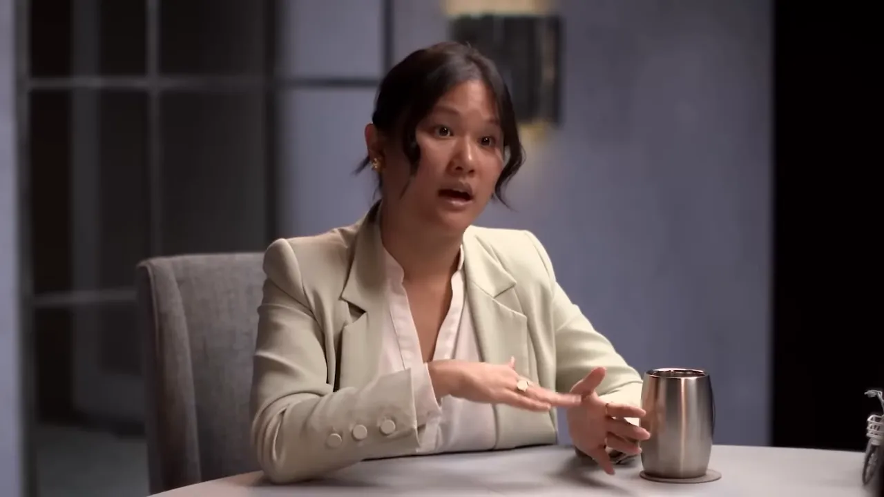 Interview speaker with both hands out while explaining managed perception in AI policy, with a can on the table