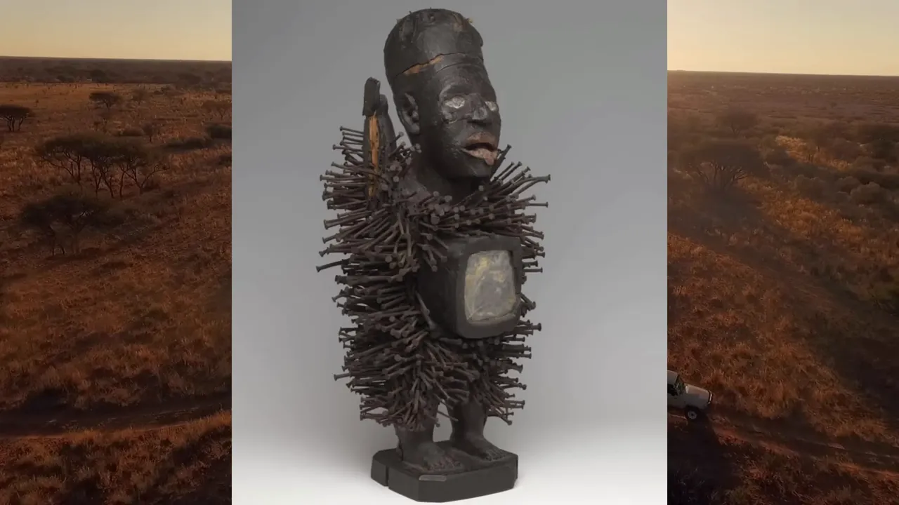 Nail-covered carved figure displayed against an aerial landscape background