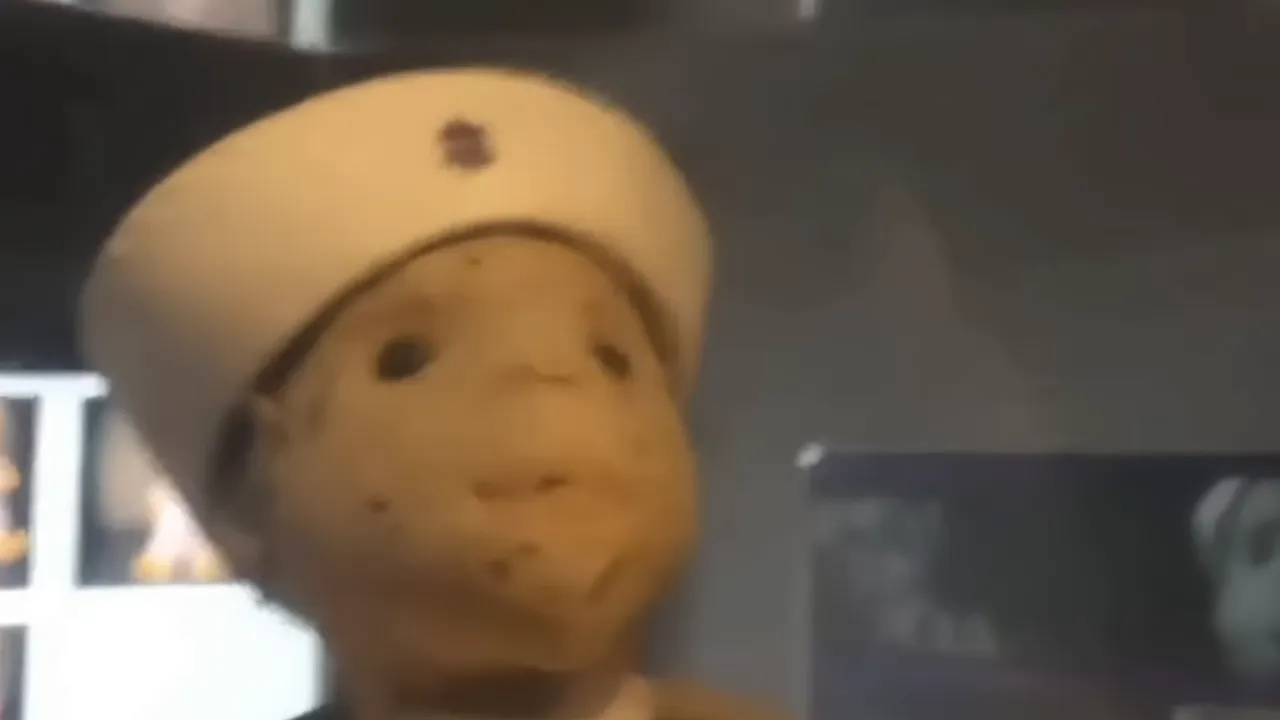 Weathered sailor doll with a cap behind museum glass