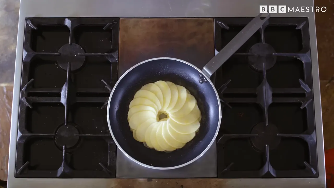 Overhead view of thinly sliced potato layers cooking in a pan for pommes Maxim
