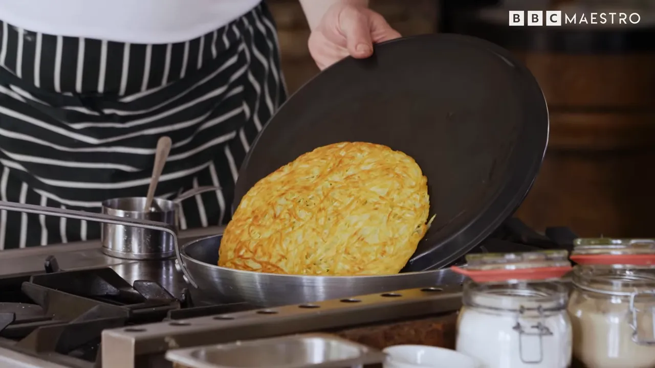 Golden potato rösti being flipped in a skillet