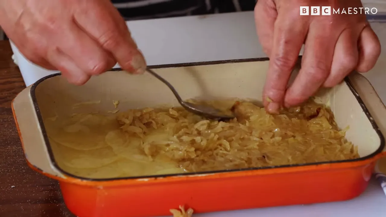 Hands pressing potato layers into a baking dish for pommes boulangère