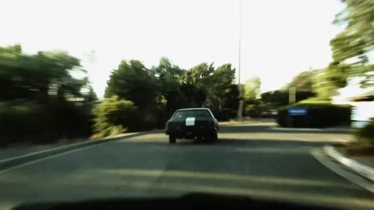 A blurred shot of a late 1970s black Oldsmobile cruising through suburban streets.