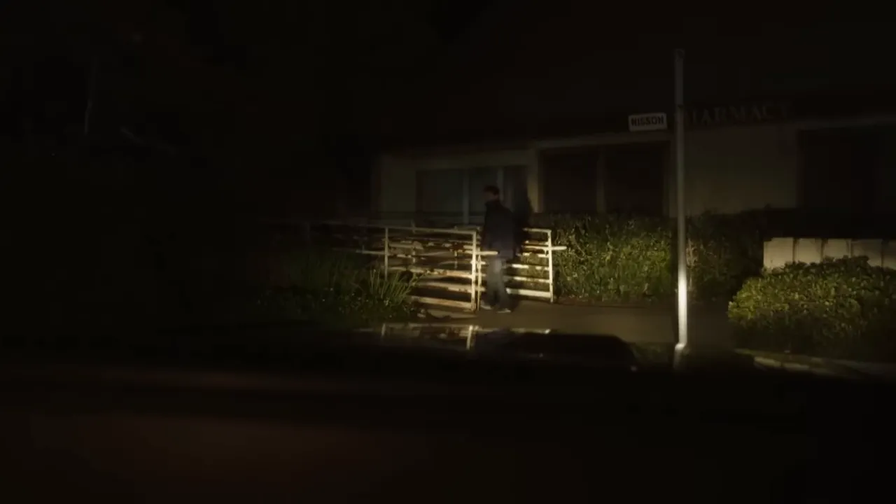 Exterior of a small-town pharmacy in the 1970s, parked cars and an evening sky.
