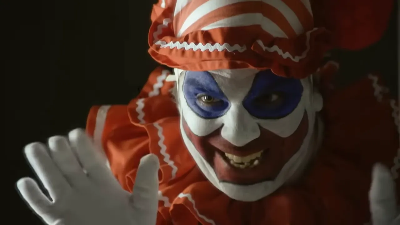 Gacy in clown costume, face painted and smiling for a photo.