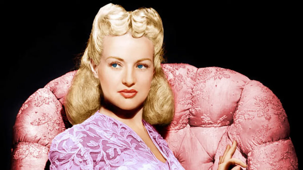 Betty Grable classic colorized studio portrait seated on a pink chair