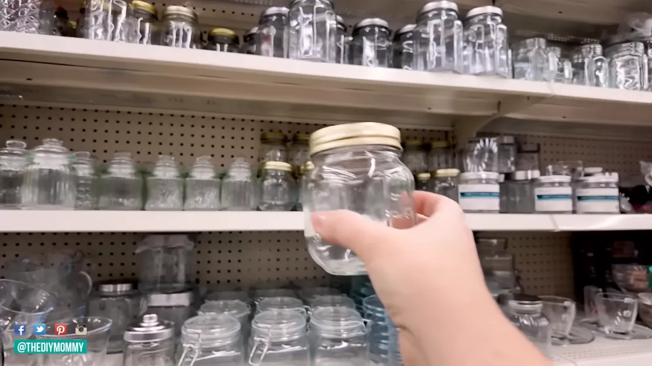 Hand holding a small clear glass jar in front of store shelves filled with jars and canisters