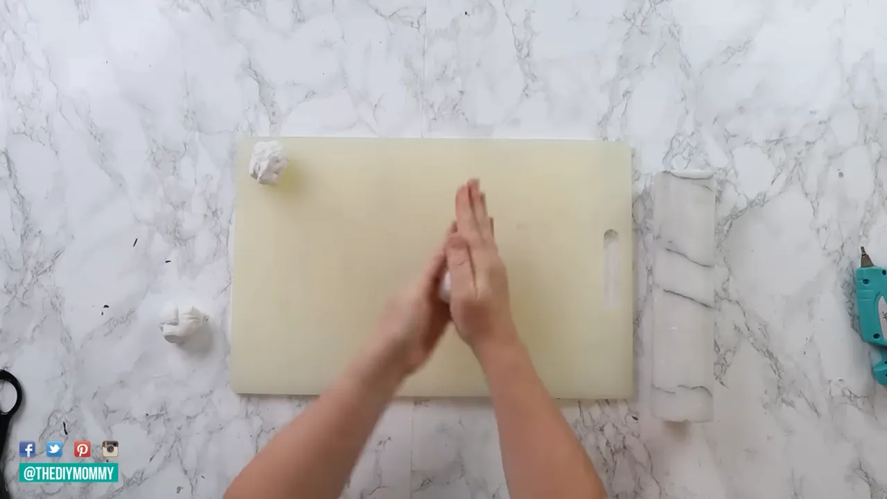 Overhead shot of hands shaping air-dry clay into a small ghost on a cutting board with crafting tools nearby