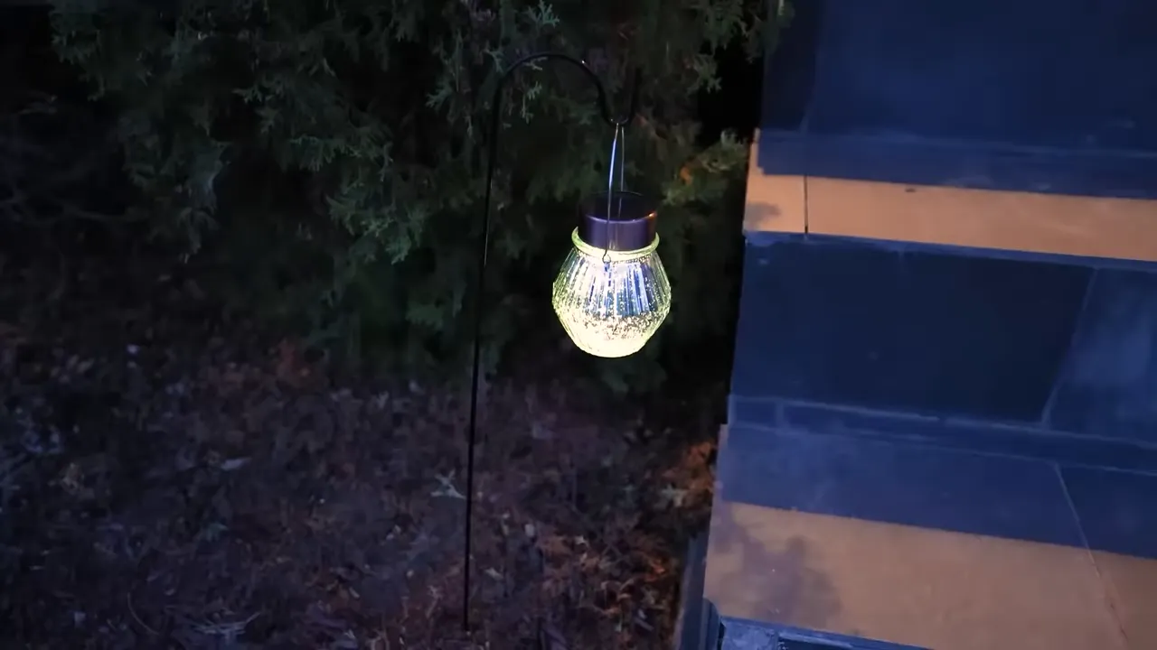 Glowing ribbed glass solar jar lantern hanging from a shepherd's hook at night beside stone steps