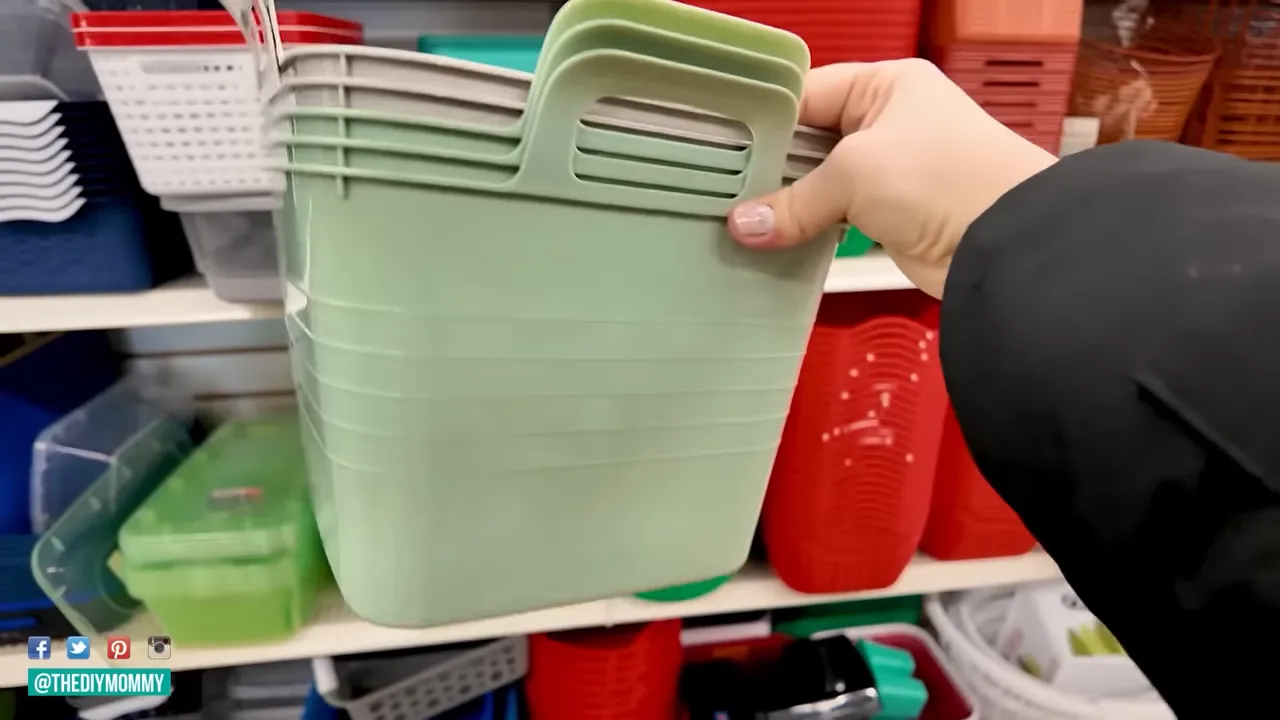 Close-up of hand holding a pale green plastic storage bin with integrated handles against store shelving of baskets
