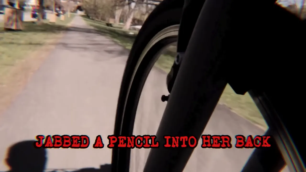 Point-of-view shot of a bicycle wheel with on-screen text 'JABBED A PENCIL INTO HER BACK'.