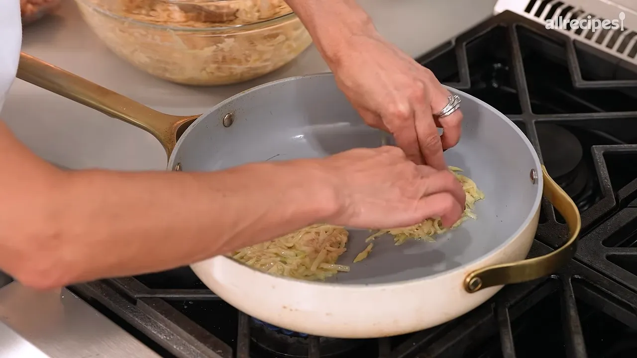 Two potato pancakes in a skillet with thin ground beef layers exposed before covering