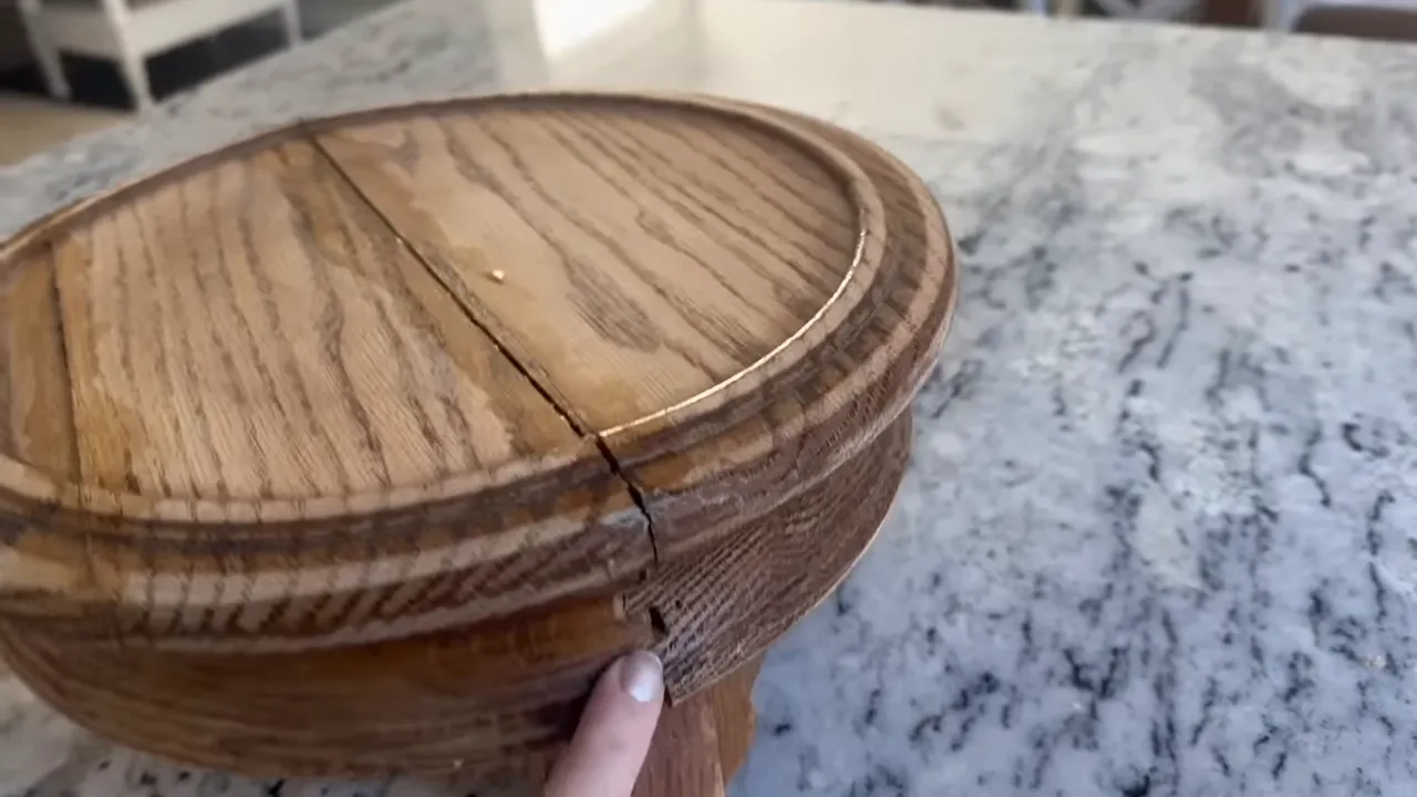Cracked oak round tabletop with a visible separation and a finger indicating the gap on a countertop