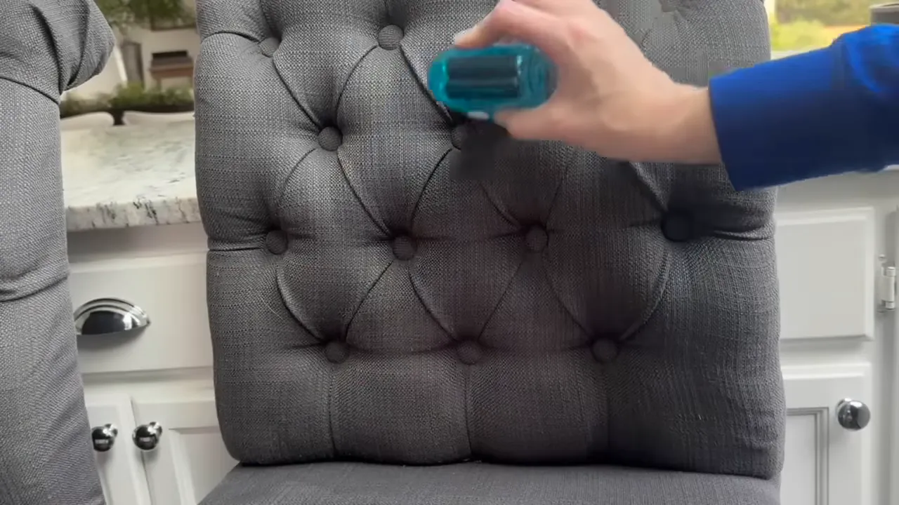Hand holding a blue fabric shaver over the tufted back of a gray upholstered chair removing pills