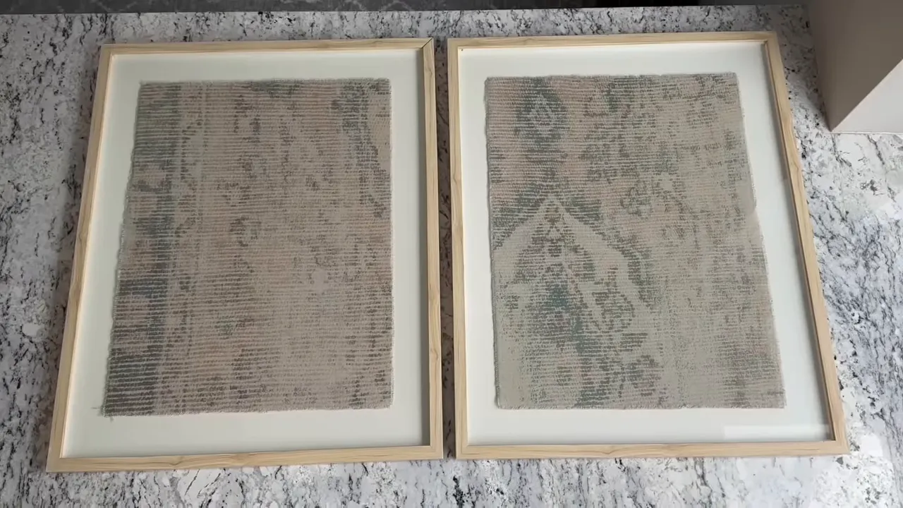 Top-down view of two framed textile panels with light wood frames and white mats on a marble countertop, showing frame edges and joints.