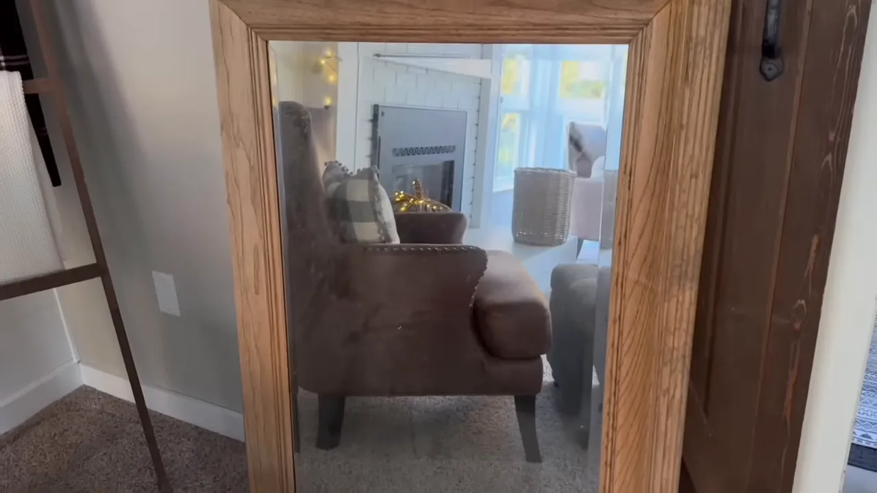 Close-up of a wooden mirror frame and its glass reflecting an armchair and fireplace, showing frame grain and edge detail