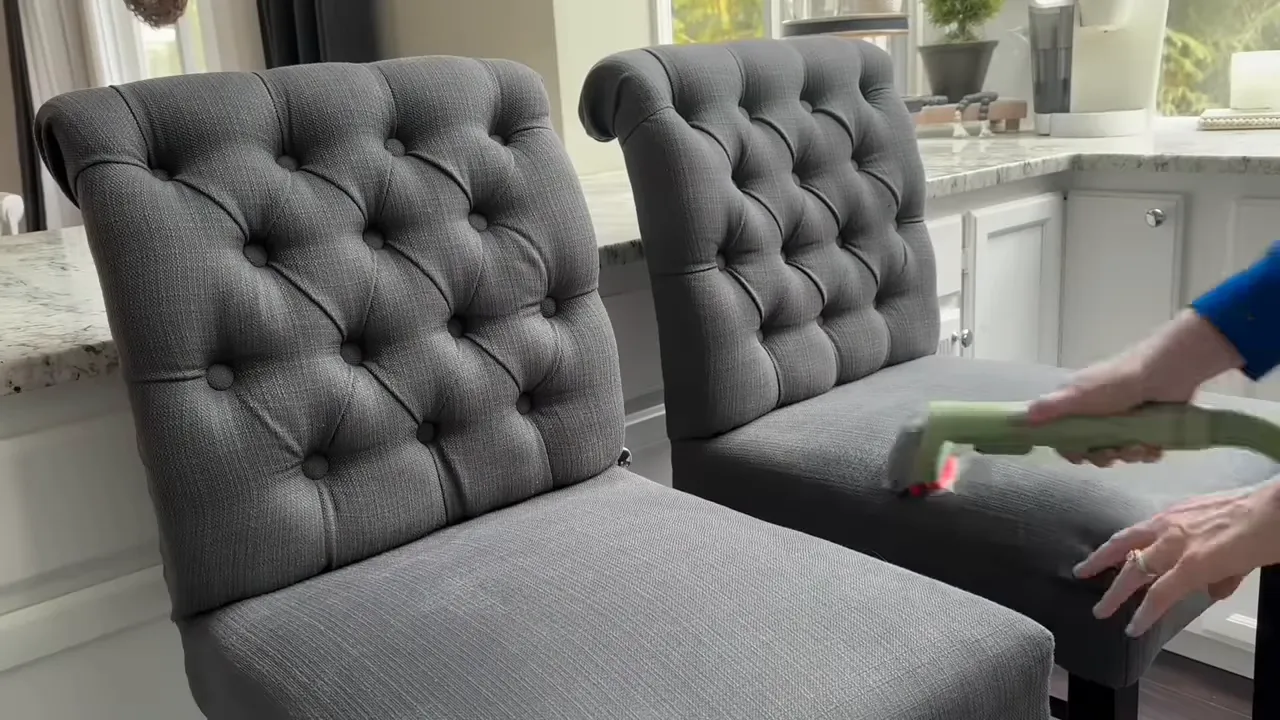 Person using a handheld upholstery cleaner on two gray tufted chairs