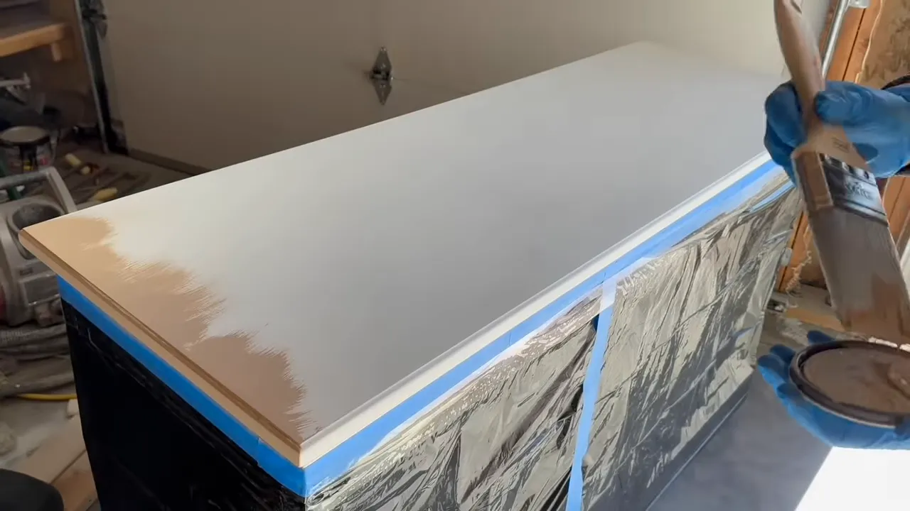 Hand in blue glove brushing Java-brown decorative glaze onto a taped dresser top to simulate wood grain