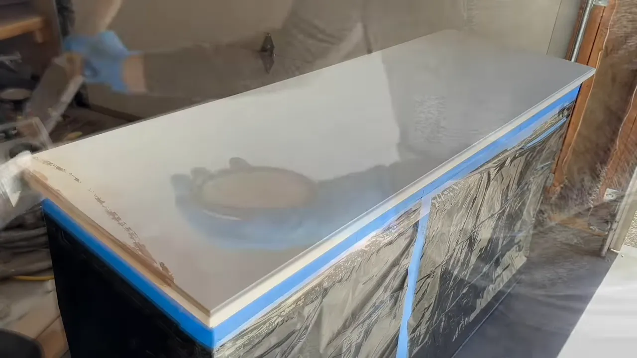 Wide view of a dresser or cabinet top freshly painted white with blue painter's tape and protective plastic on the sides