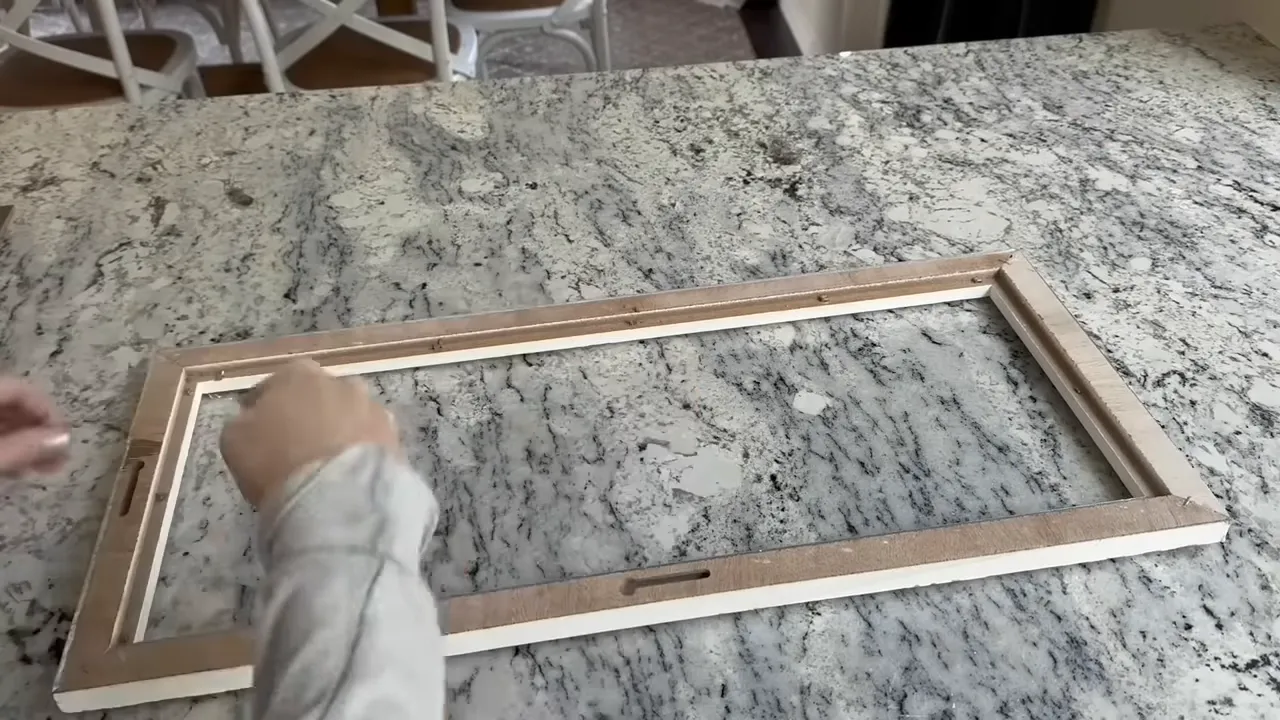 Wooden picture frame laid flat on a marble countertop with hands reaching in to position it