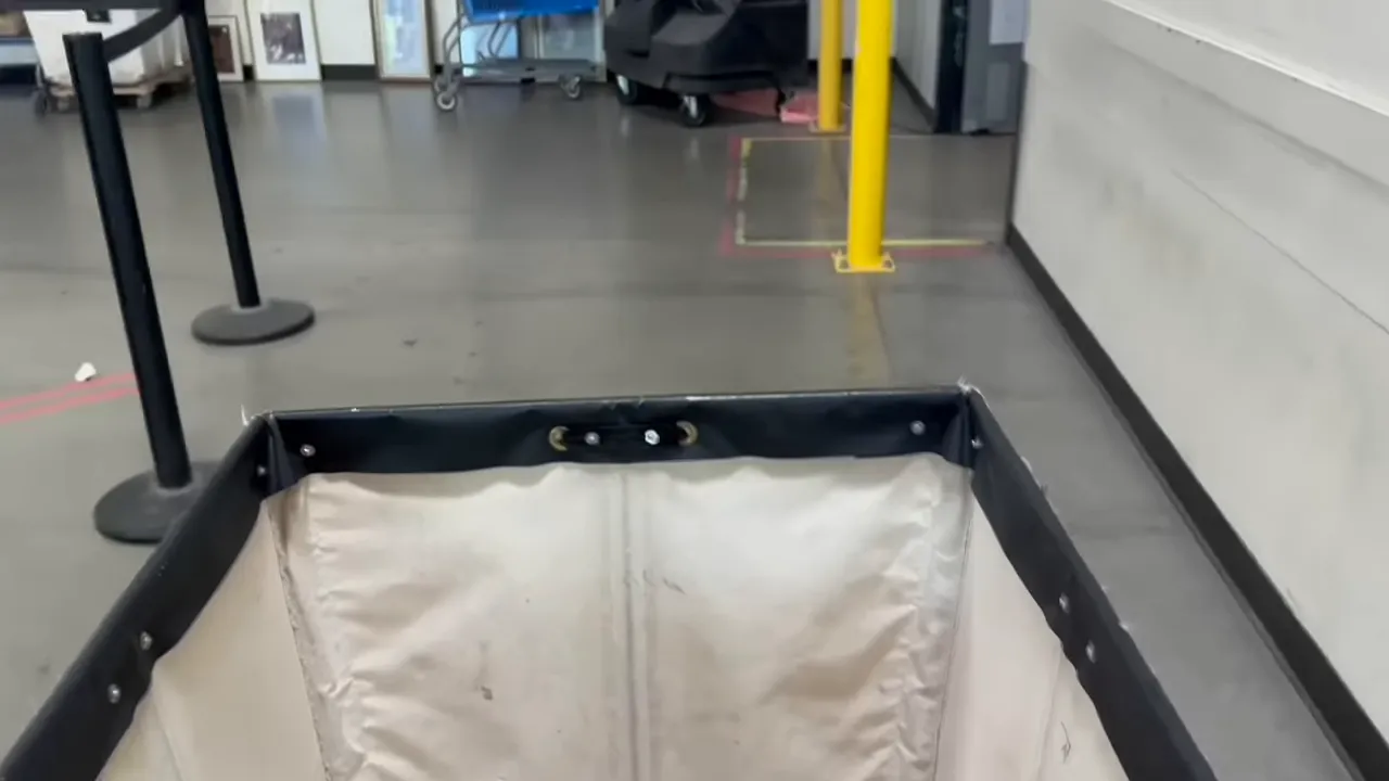 Canvas cart liner and warehouse floor inside a thrift outlet, with stanchions and a yellow safety post