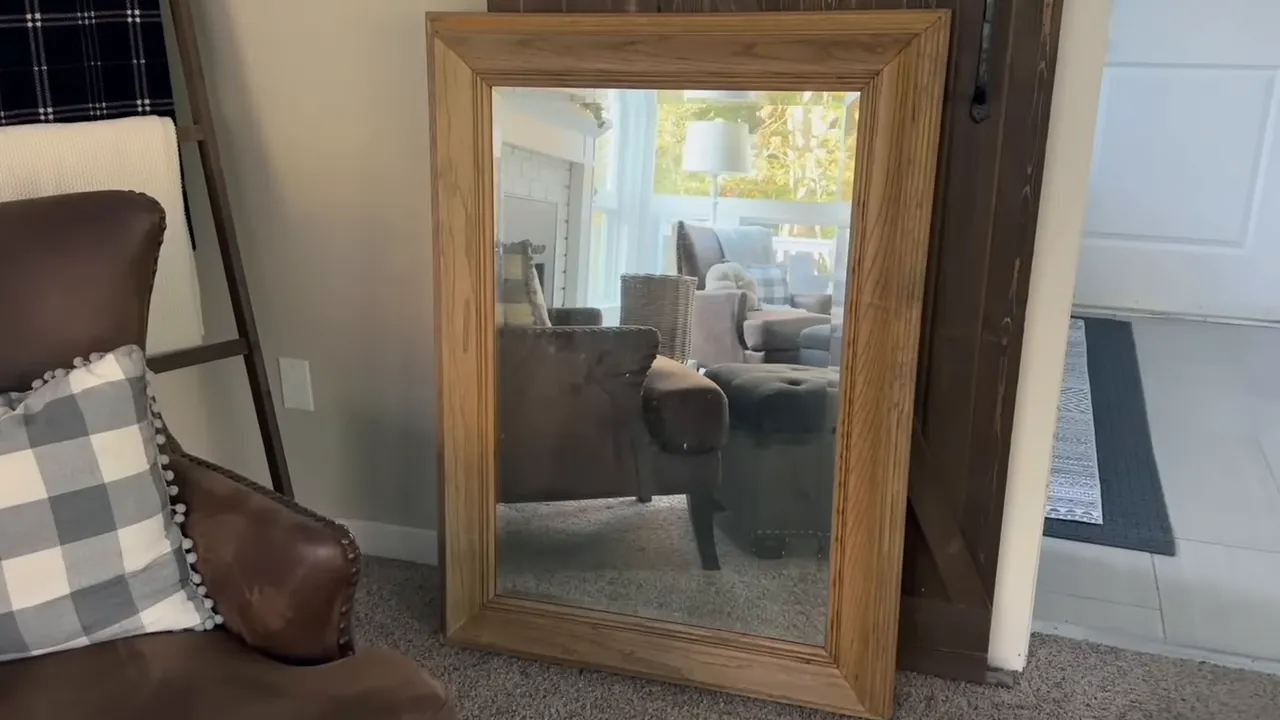 Full-length oak framed mirror leaning against a wall reflecting a living room scene