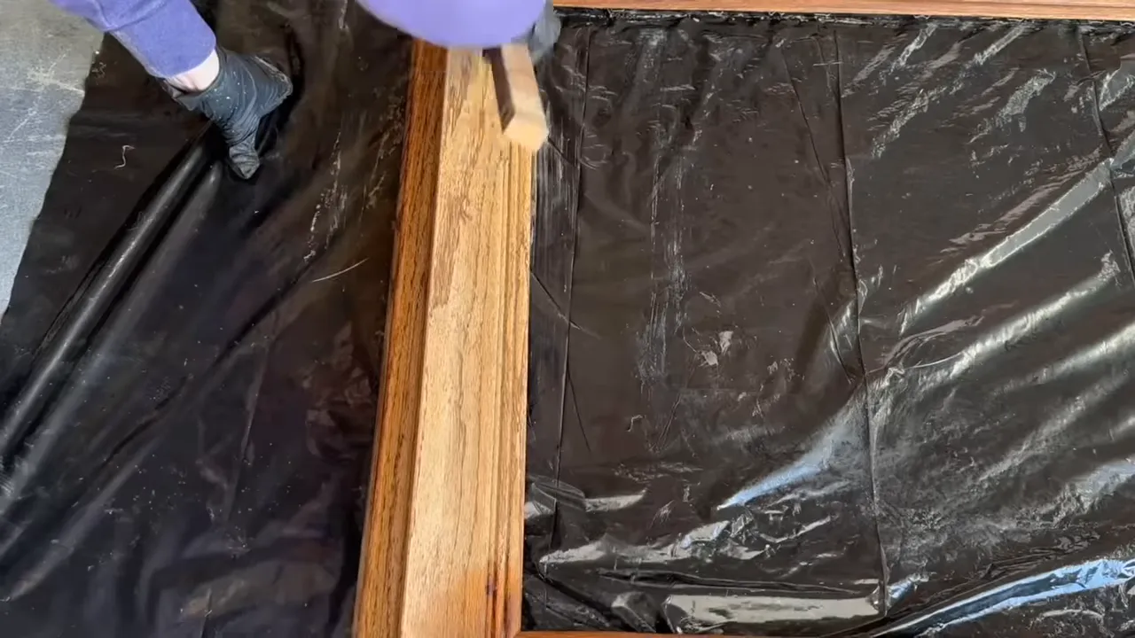Person in gloves brushing an oak frame to accentuate the wood grain on a black drop cloth