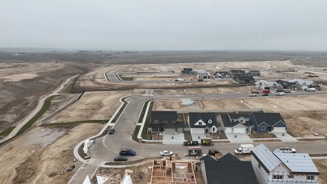 Wide aerial overview of Mayfield Springs development with new homes, streets, and vacant lots.