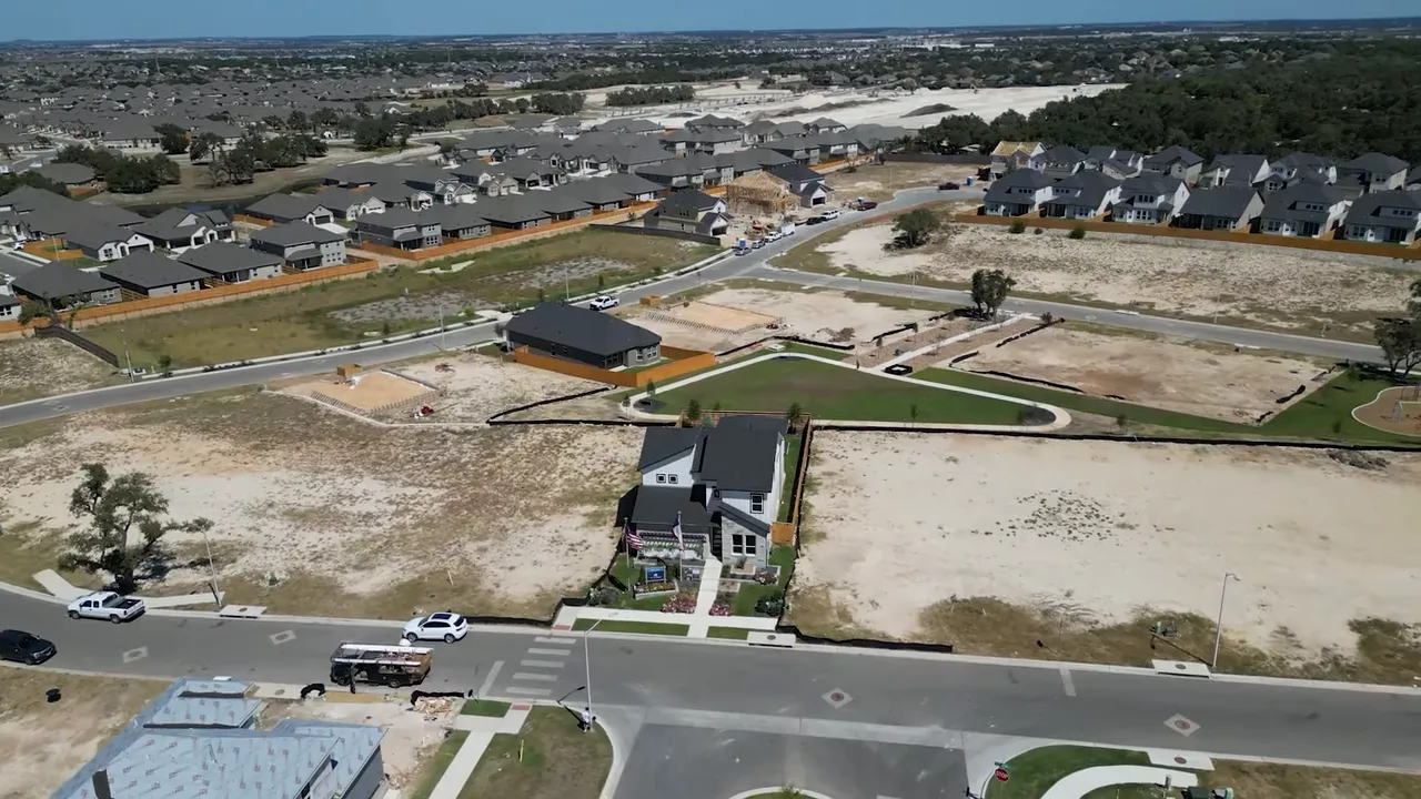 Drone shot of a new neighborhood with a single model home, surrounding vacant lots and visible construction areas