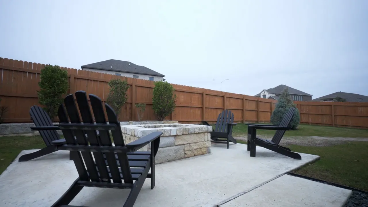 Backyard patio seating area with paver wall and wooden privacy fence in a Buda TX new construction home