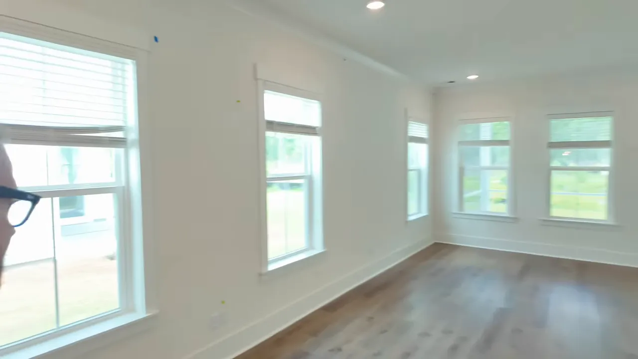 Open living room with wood-look flooring white walls and multiple windows