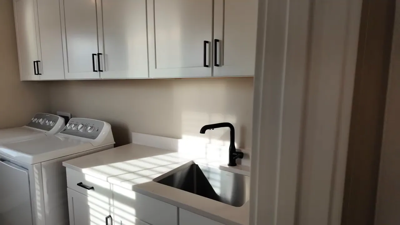 Bright laundry room showing washer and dryer, quartz countertop with undermount sink and white cabinets