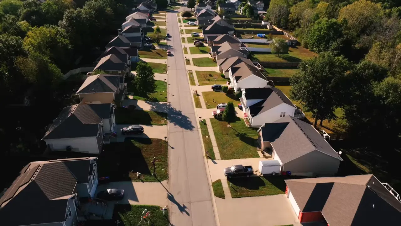 Clear drone image looking down a residential street with matching single-family houses, driveways, and tree-lined backyards in Fountain Hills.