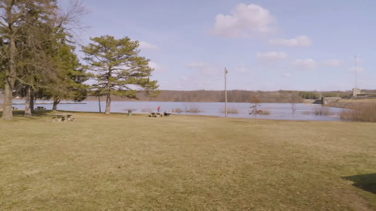 Open grassy park area beside reservoir with trees and water in background