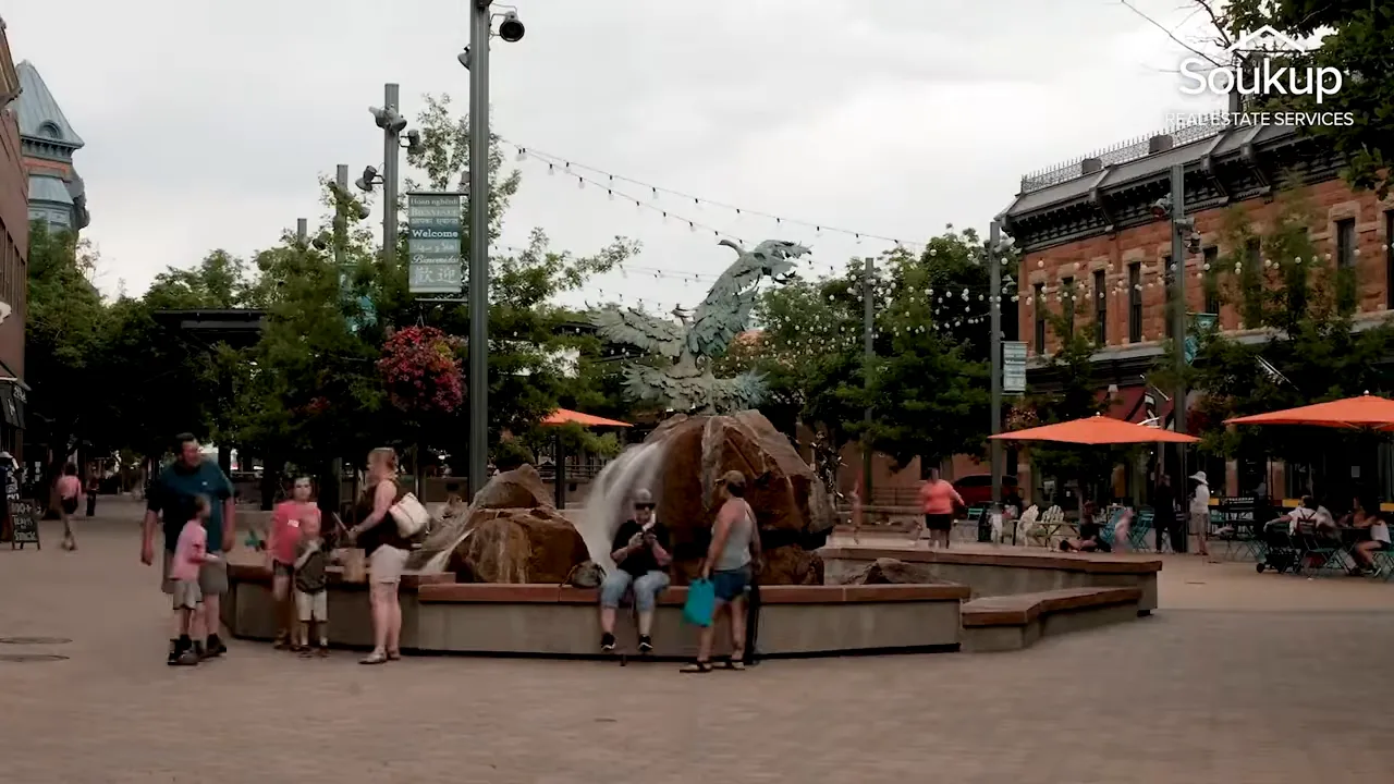 People gathered in Old Town Fort Collins plaza with fountains and brick buildings