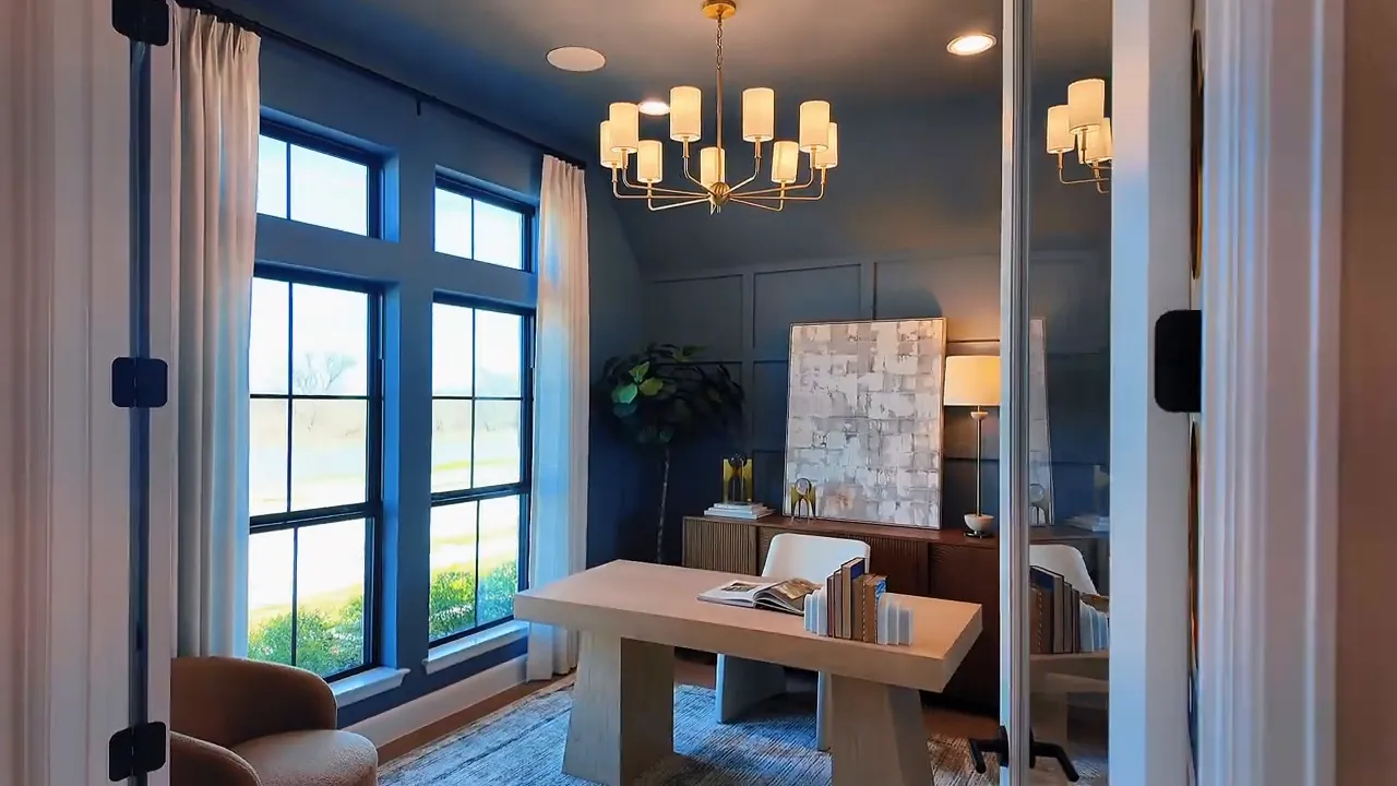 Bright home office with large windows, chandelier, and neutral design accents in Meraki by Perry Homes Forney Texas