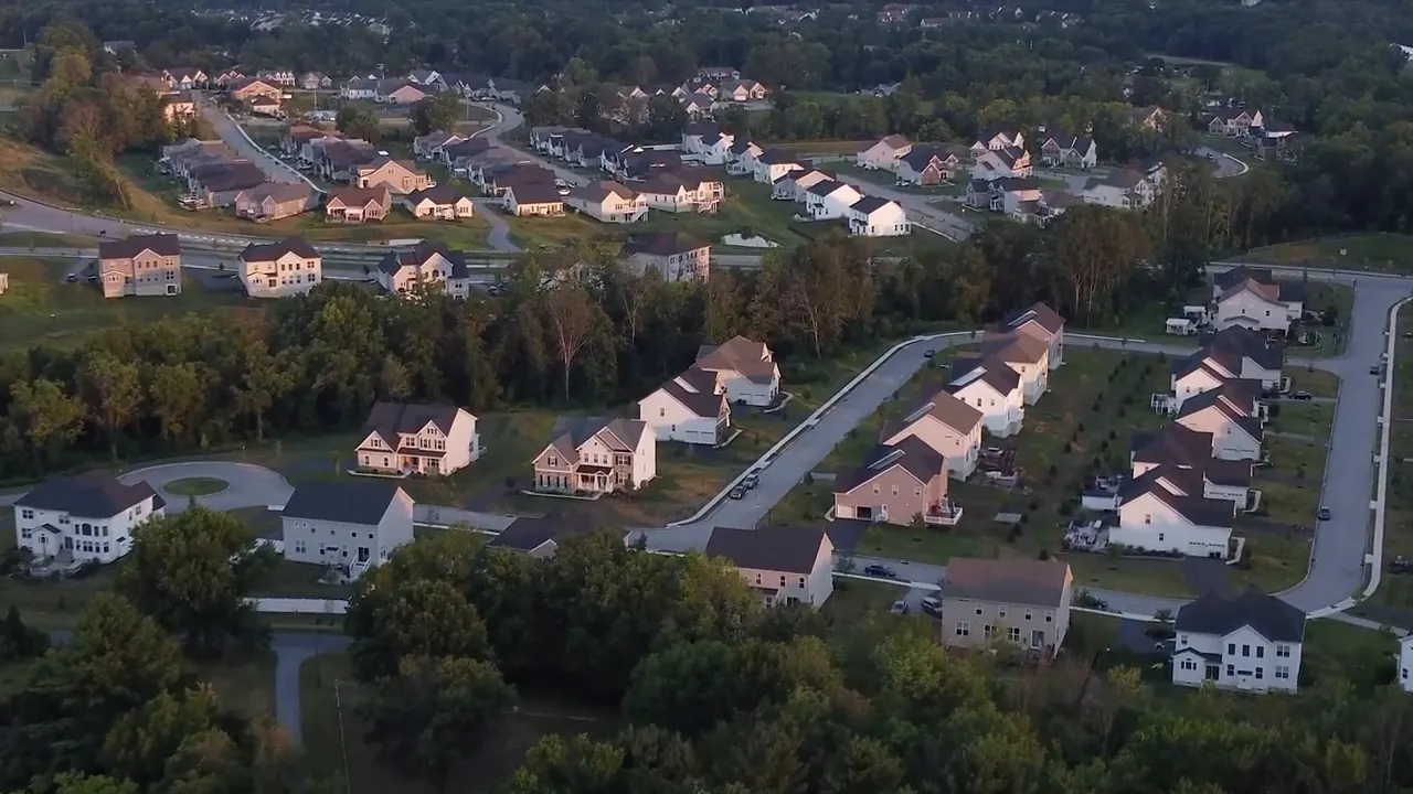 Wide drone shot of a suburban neighborhood with repeated house designs and roads illustrating a single-builder development